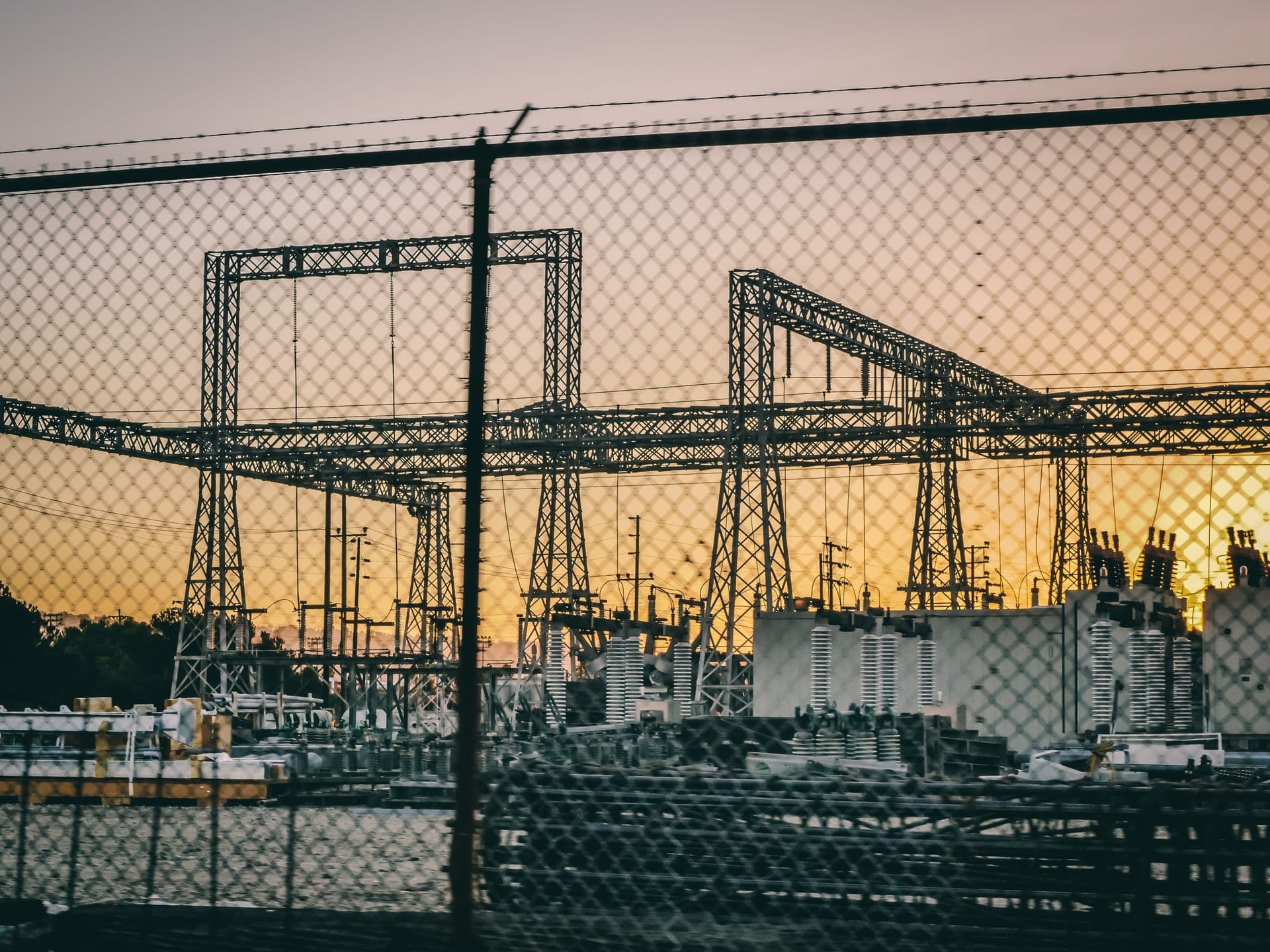 High-voltage substation gantries and transformers silhouetted at sunset